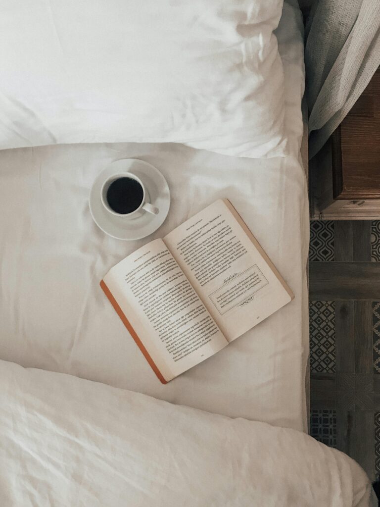 Libro y taza de café sobre una cama, representando un momento de relajación y disfrute en casa.