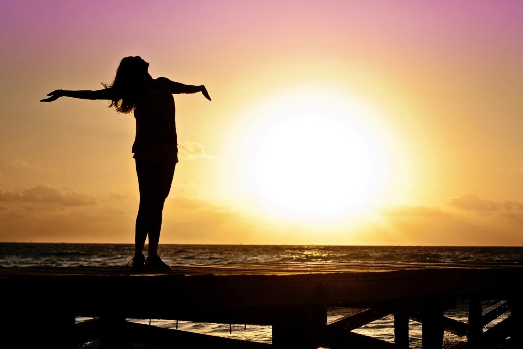 una mujer disfrutando de un atardecer en la naturaleza, simboliza la conexión con el entorno y la tanquilidad. 